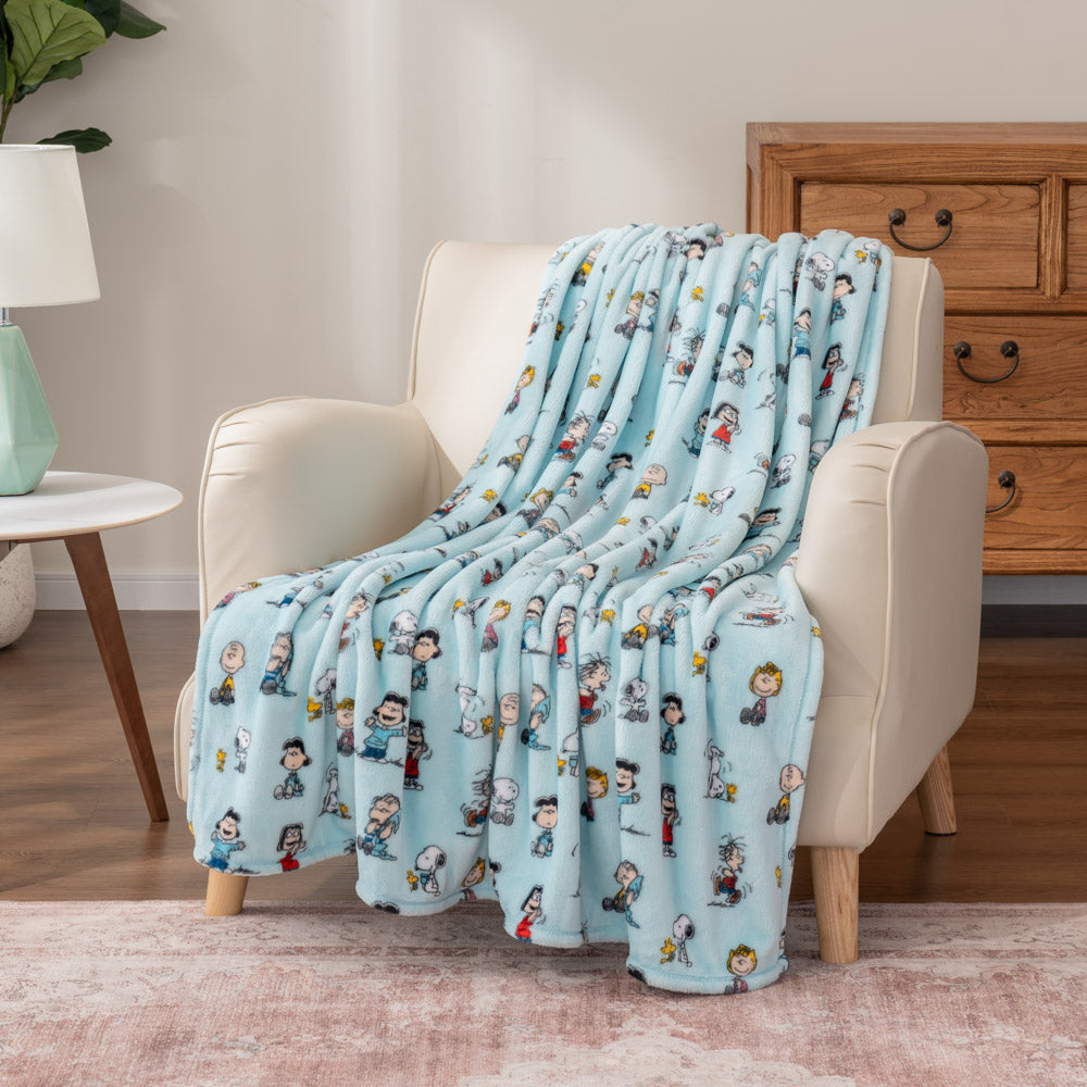 A light blue throw blanket with Snoopy, Woodstock, and scattered characters draped over an armchair.