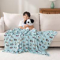 A child sitting in a room holding a snoopy toy, wrapped in a light blue throw blanket with Peanuts character prints.