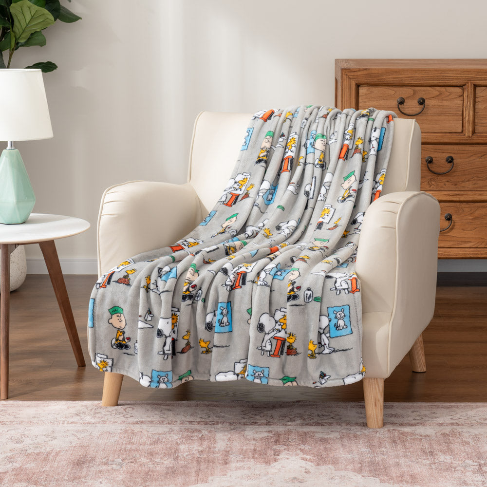 Gray cartoon-patterned blanket draped over a beige armchair in a living room setting.