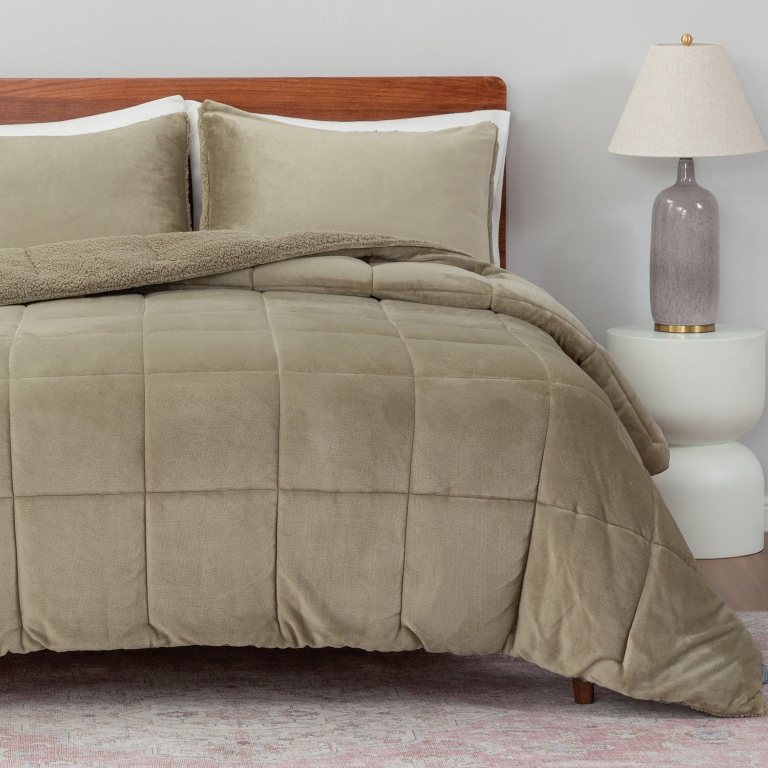 Beige comforter set on a bed with pillows and a lamp in the background