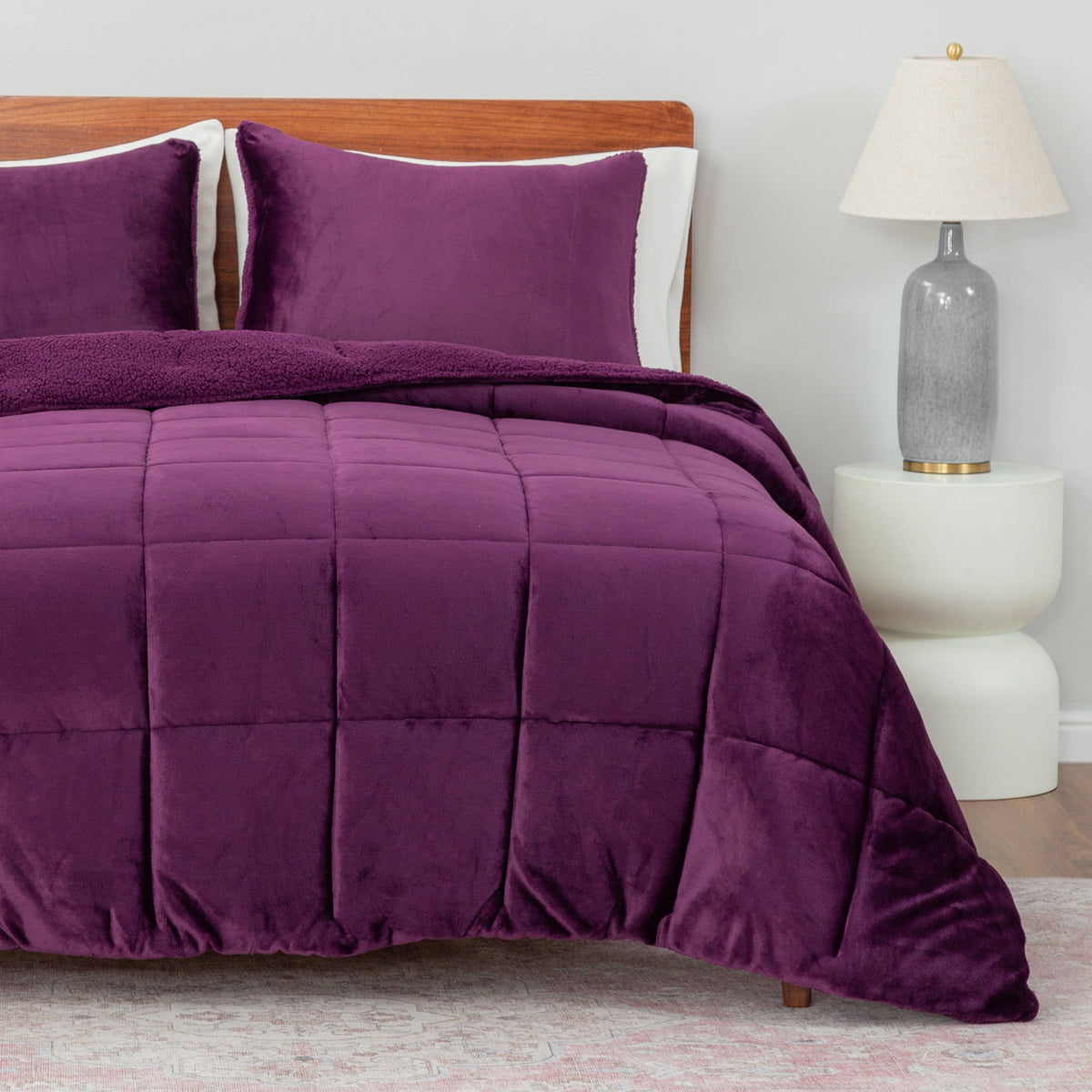 Purple comforter set on a bed with a wooden headboard and white nightstand.