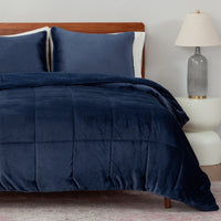 Navy blue comforter set on a bed with pillows and a lamp in the background.