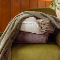 Folded blankets in beige and brown on a green chair with a wooden wall background