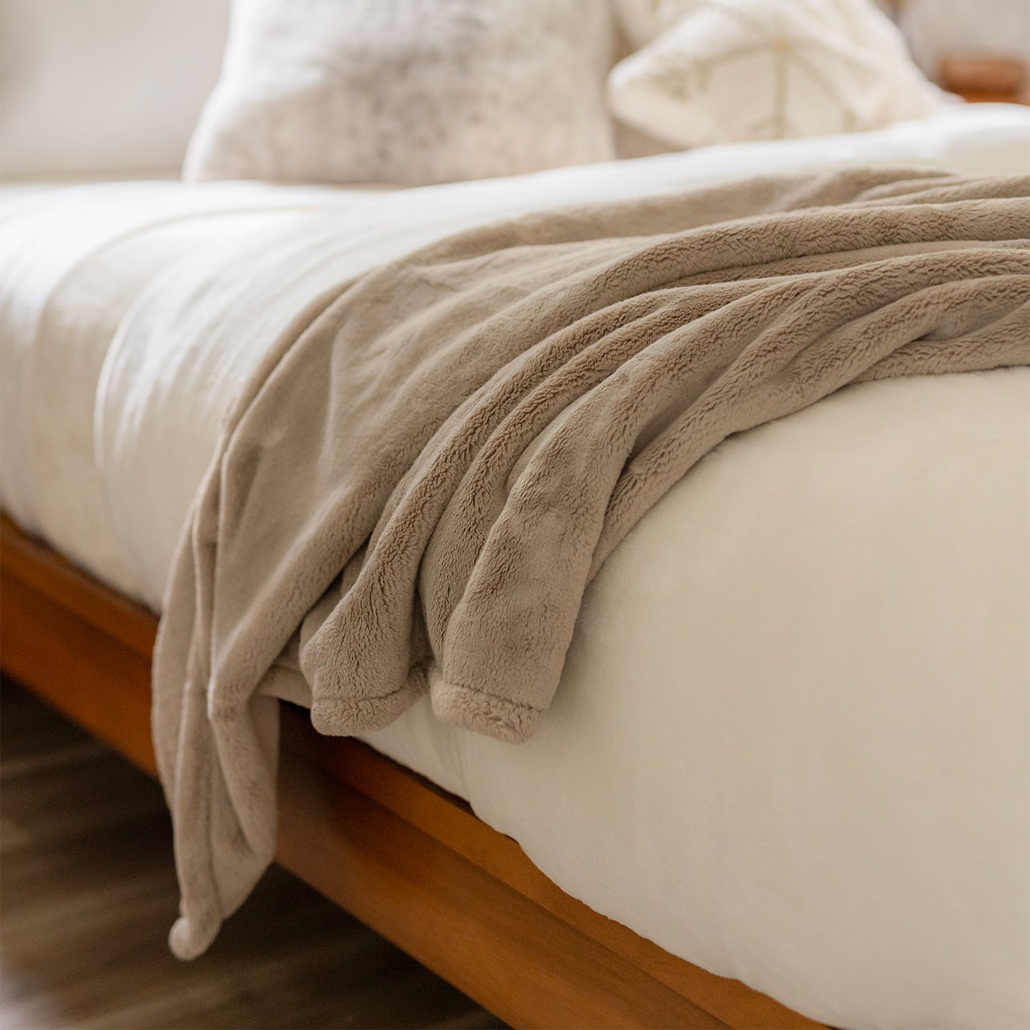 A tan throw blanket draped over a white bed.