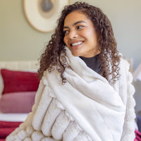 Woman wrapped in a white blanket, smiling in a cozy living room.