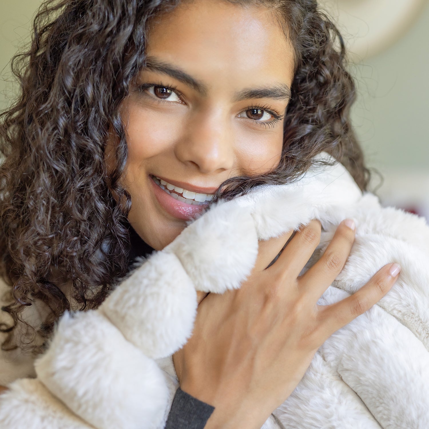 Woman holding a white fluffy blanket with a soft smile