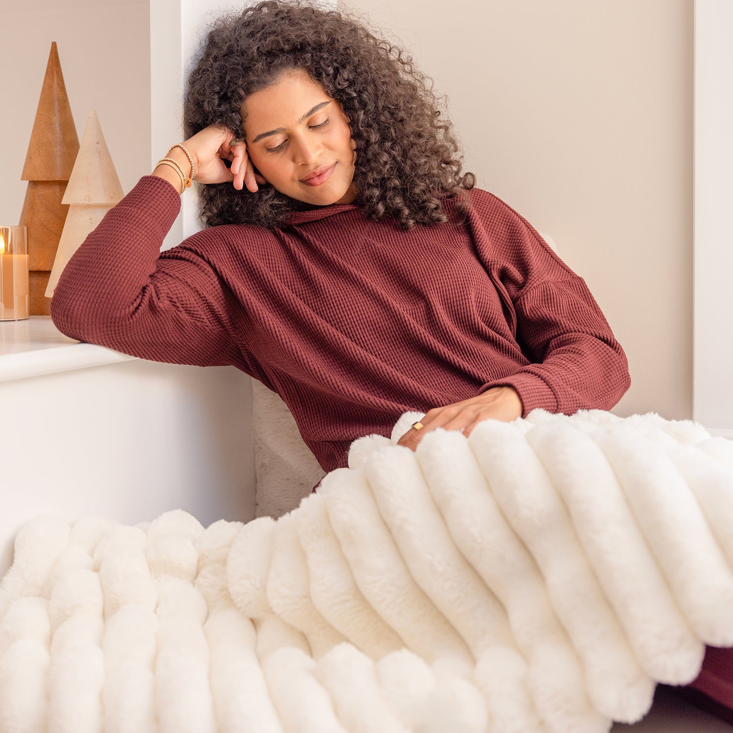 Woman in a maroon sweater sitting on a bed with white bedding