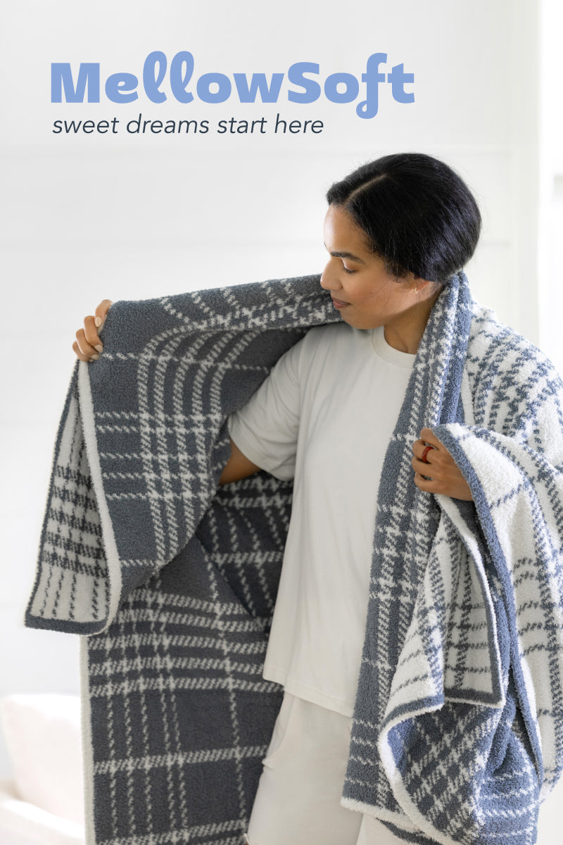 MellowSoft - sweet dreams start here. image of a woman wearing a plaid blue and white throw sound her shoulders with her arms spread open to show how stretchy and luxe MellowSoft is. 