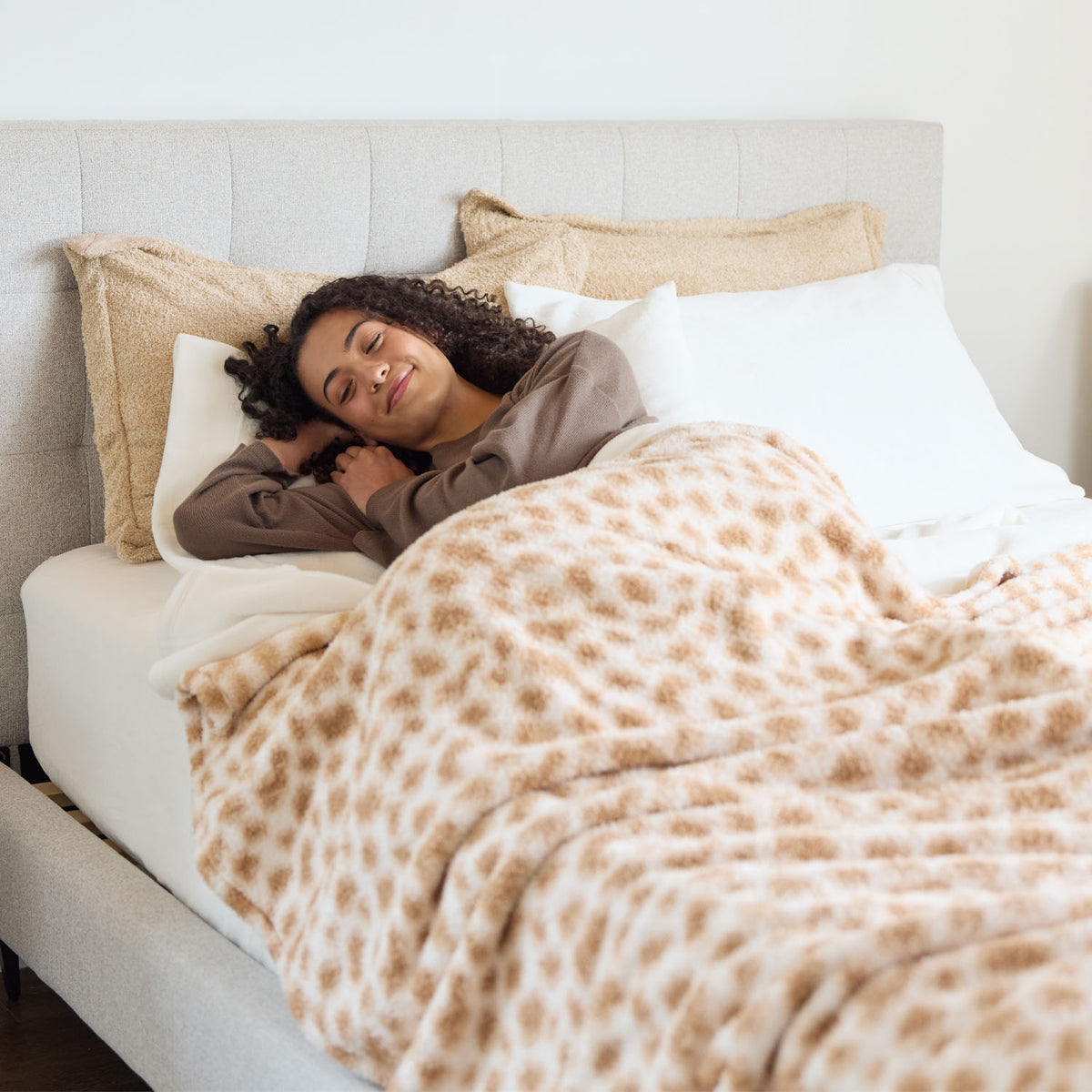 Woman lying in bed under a patterned blanket, smiling.