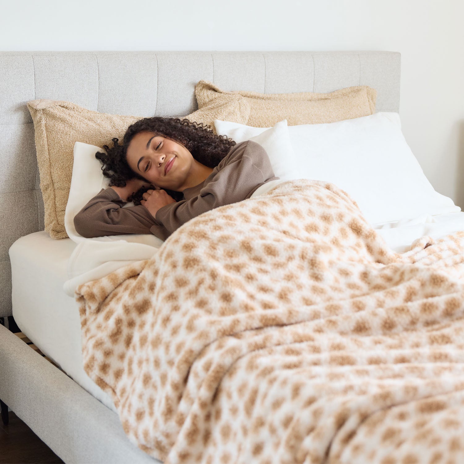 Woman lying in bed under a patterned blanket, smiling.