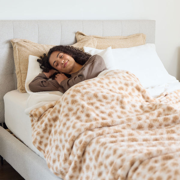 Woman lying in bed under a patterned blanket, smiling.