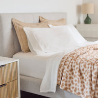 Neatly made bed with white pillows and a leopard print blanket next to a wooden nightstand.